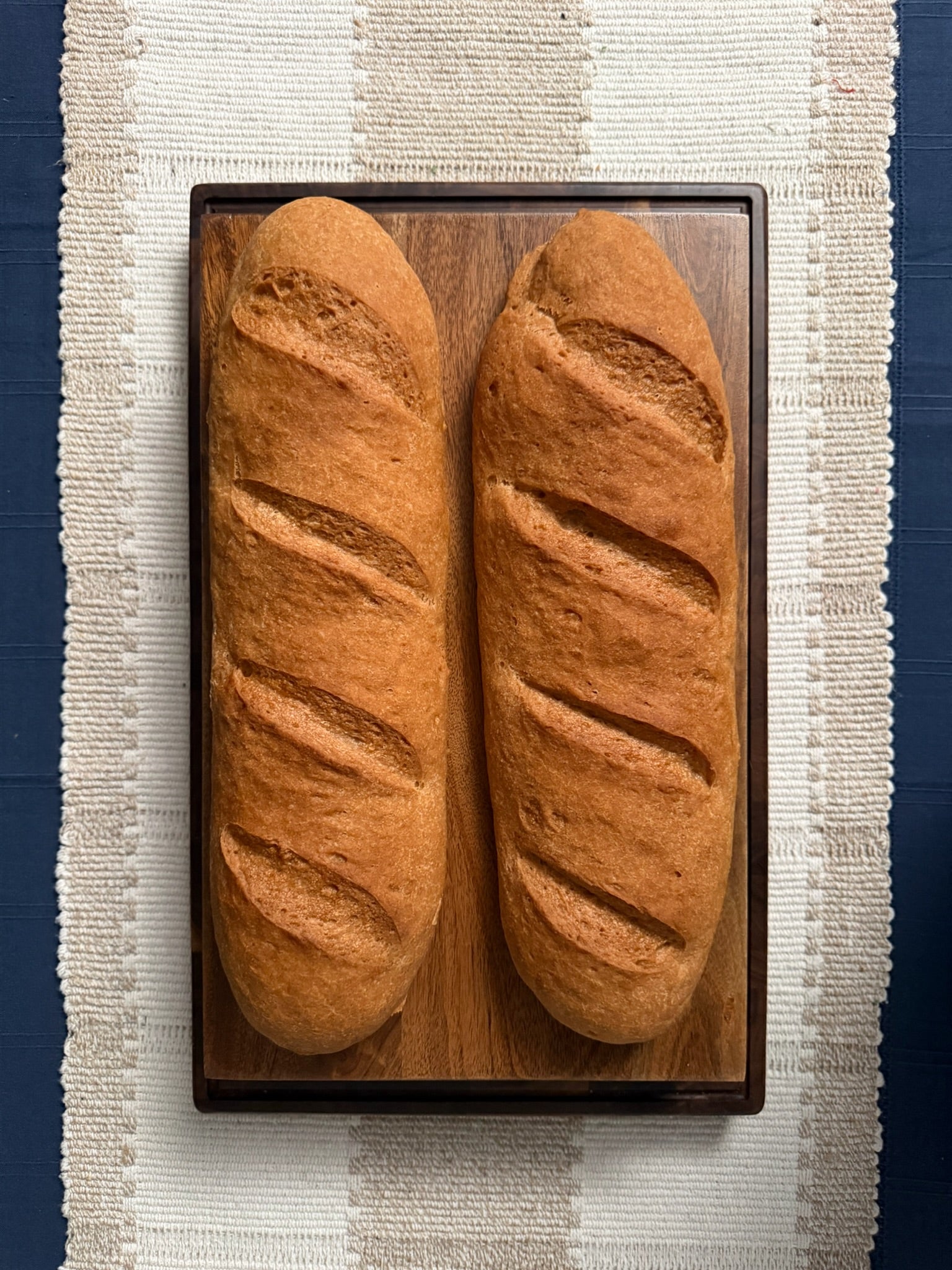 Two loaves of gluten free french bread on a wooden cutting board with a striped background
