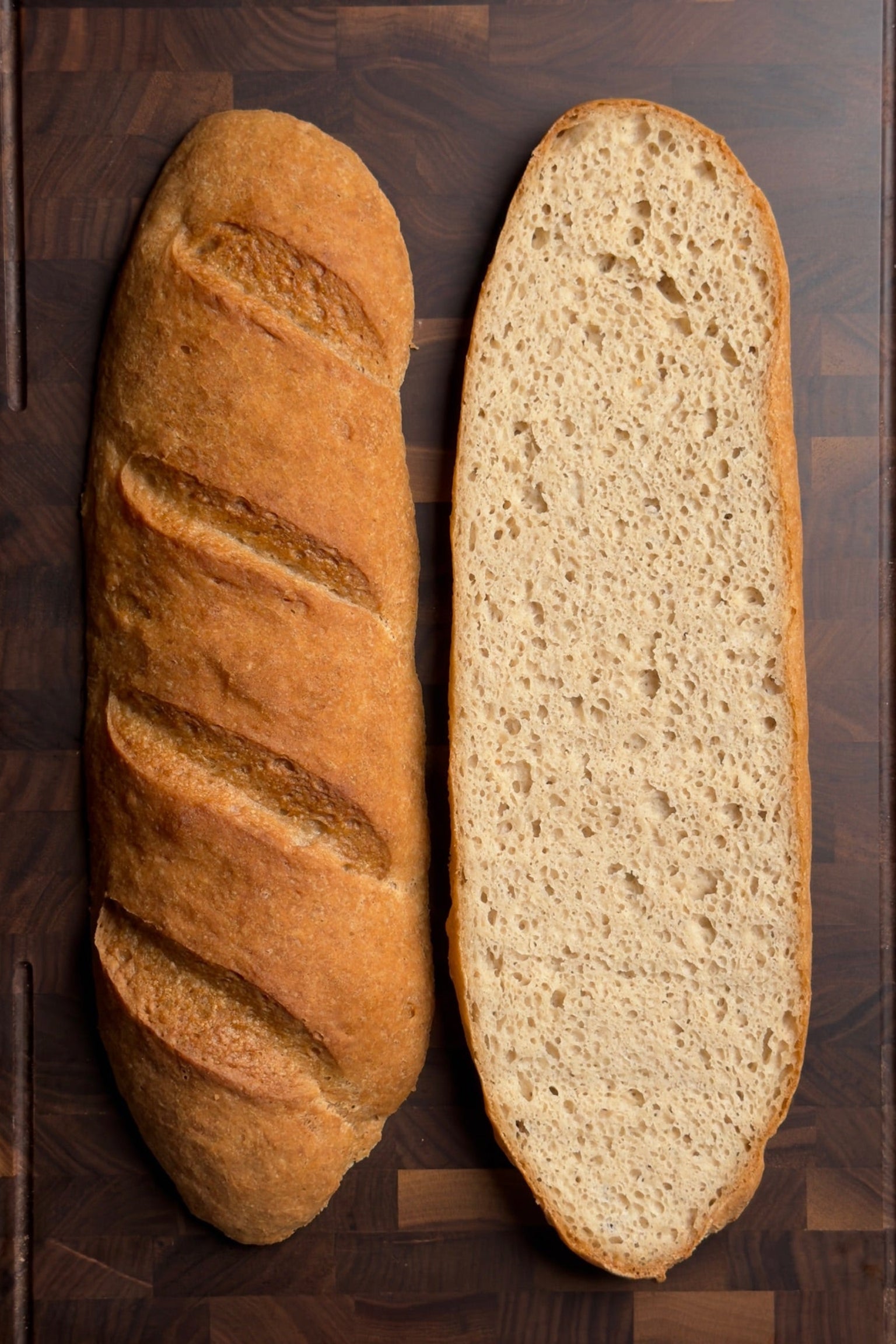 Two loaves of bread on a wooden surface, one whole and one sliced open.