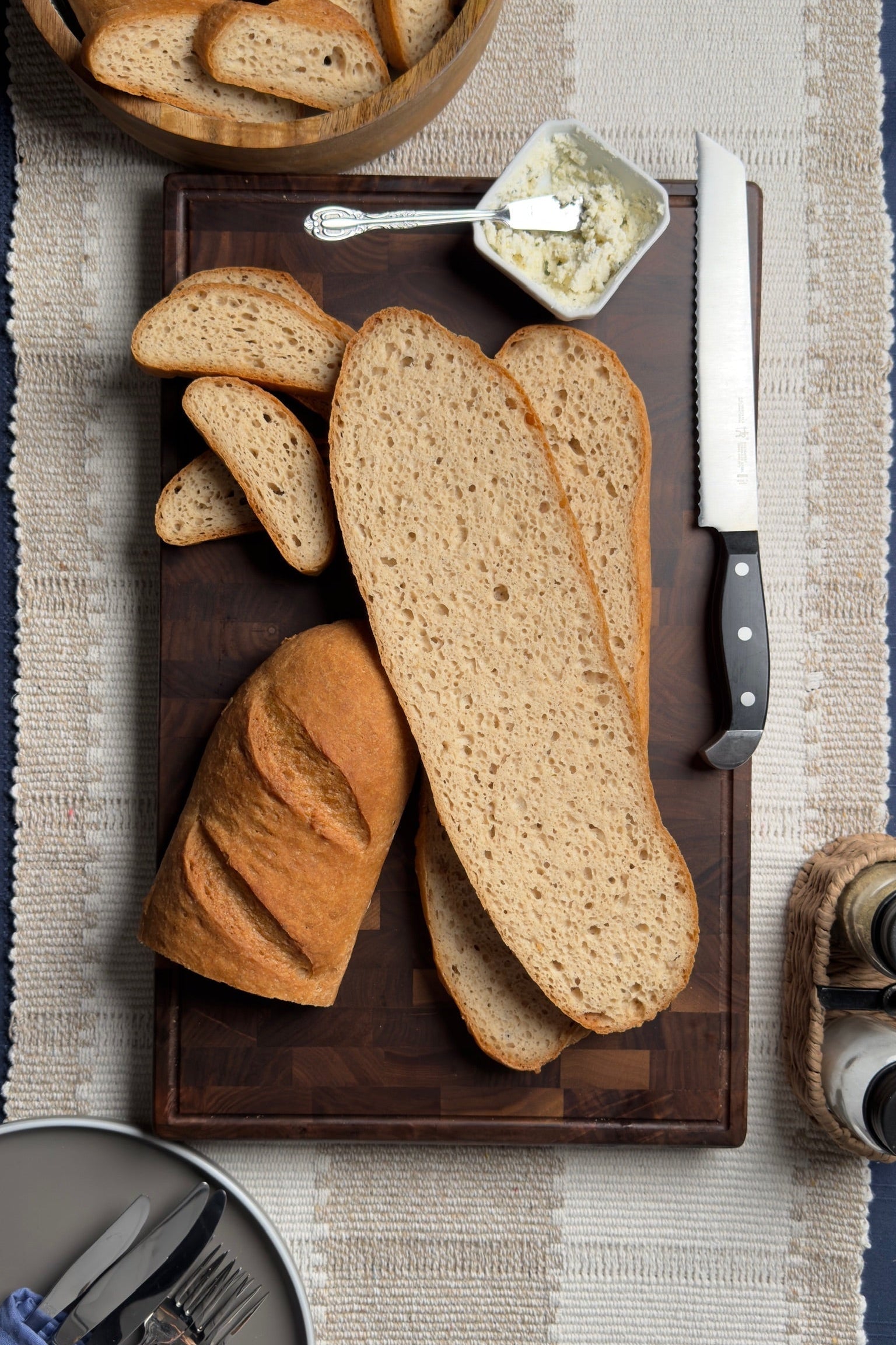 Gluten free french loaves of bread on a wooden cutting board with a knife and butter dish.